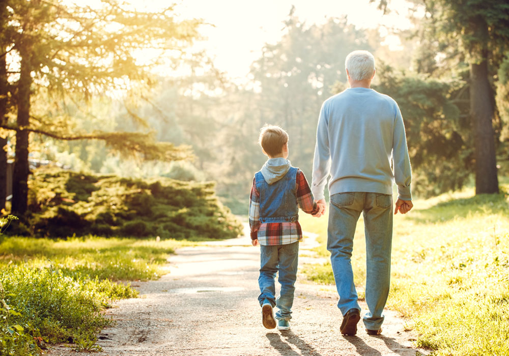 child and adult walking hand in hand through a park 